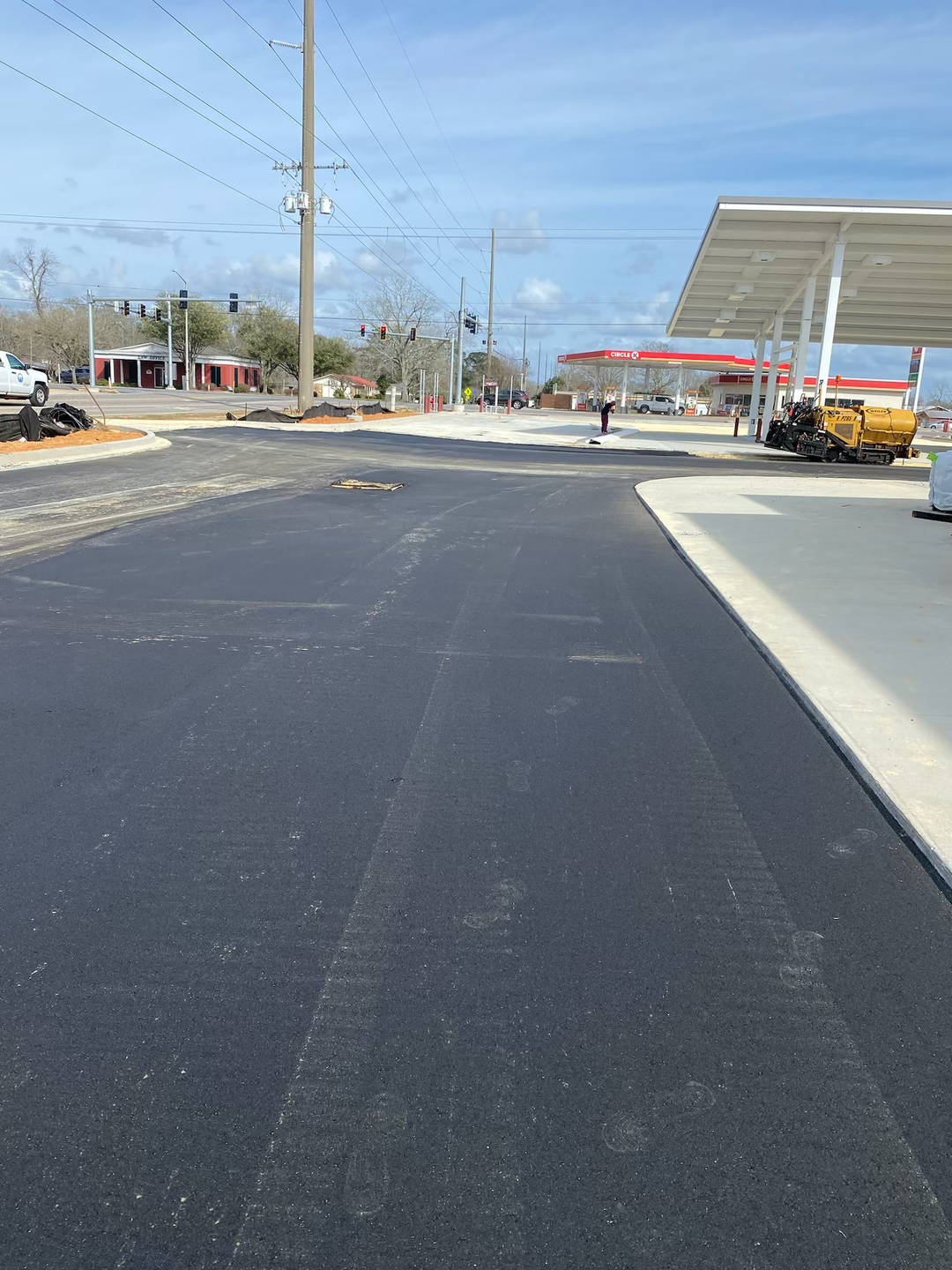 Fresh asphalt paving and concrete work around a commercial access drive and fuel station