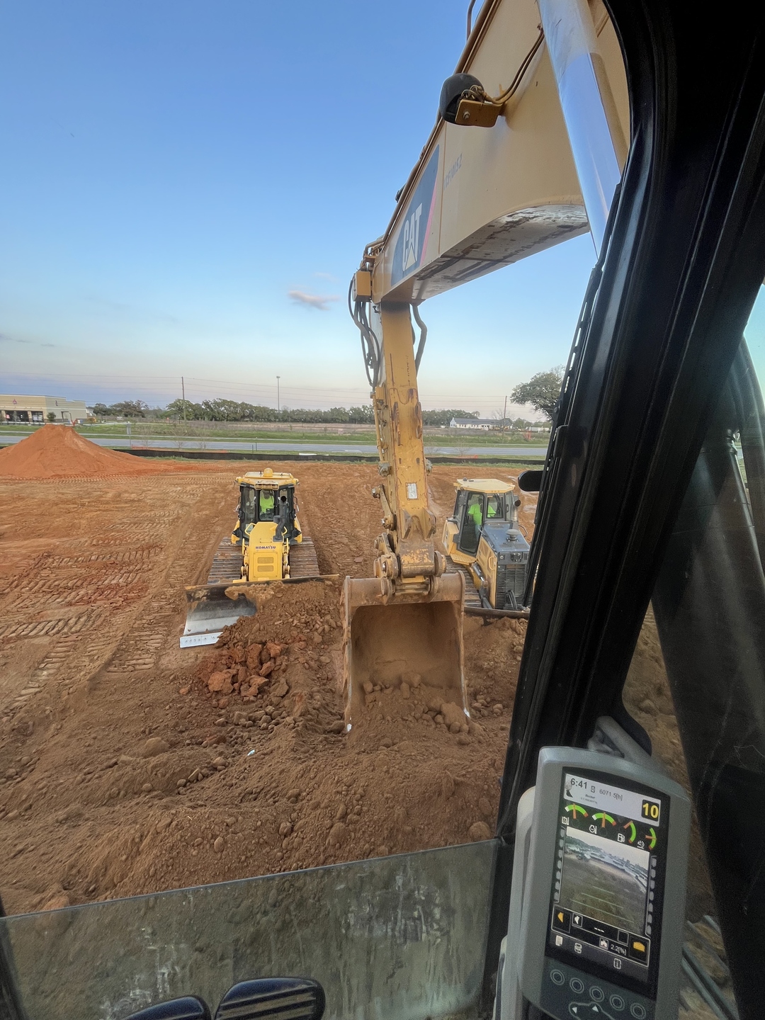 Excavator cab view with machine control display while grading a large site